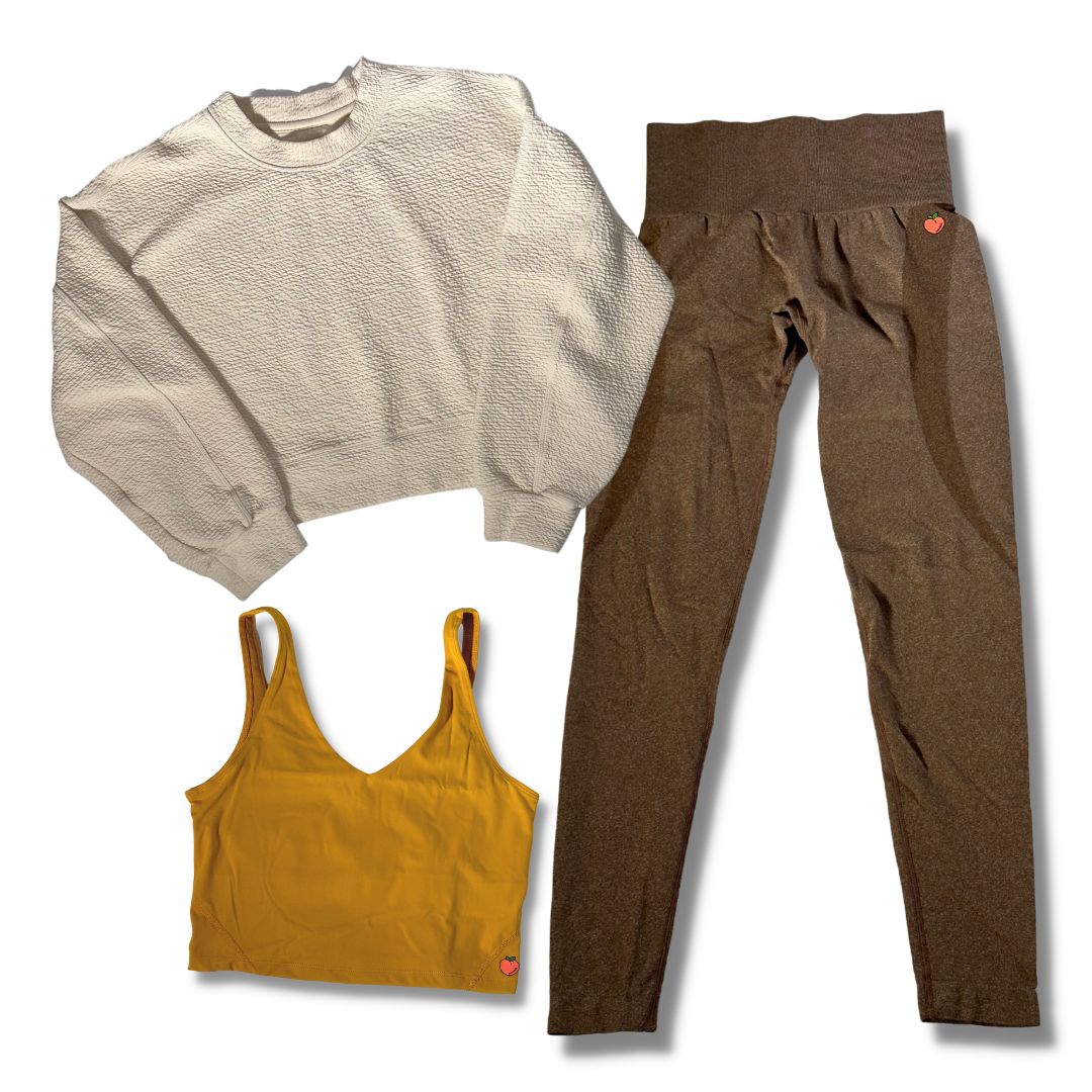 The image features a laid-out ensemble of athleisure wear against a white backdrop, consisting of a vanilla bean-colored crewneck sweater, a mustard sports bra, and brown joggers. Each piece is showcased to emphasize its color and design.